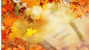 An autumn-themed scene with falling leaves in vibrant orange and yellow hues, a gratitude journal open with handwritten text, and a wooden pen resting on the page.